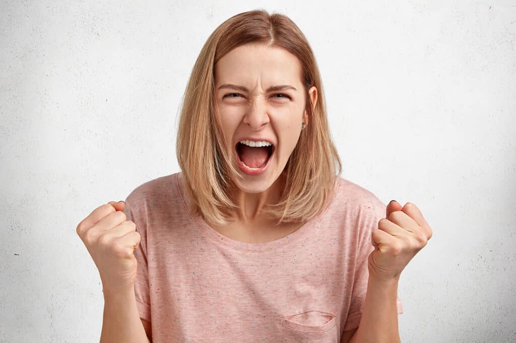 People And Aggression Concept. Irritated Young Female Model With Bobbed Hairdo, Dressed In Casual Clothing, Clenches Fists In Anger, Has Quarrel With Husband, Poses In Studio Againt White Background