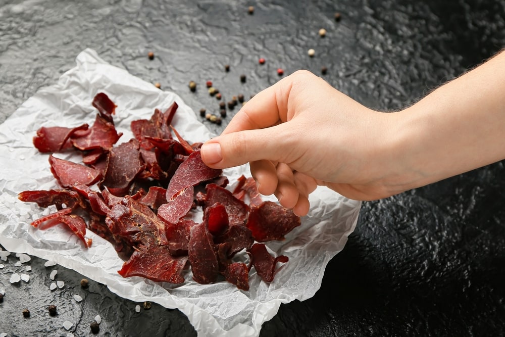Woman,eating,spicy,beef,jerky,on,dark,background