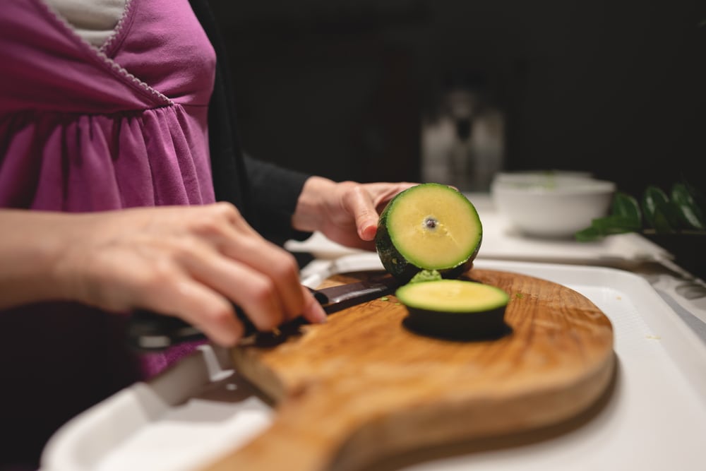 Woman,cutting,avocado,on,a,wooden,board,with,a,knife